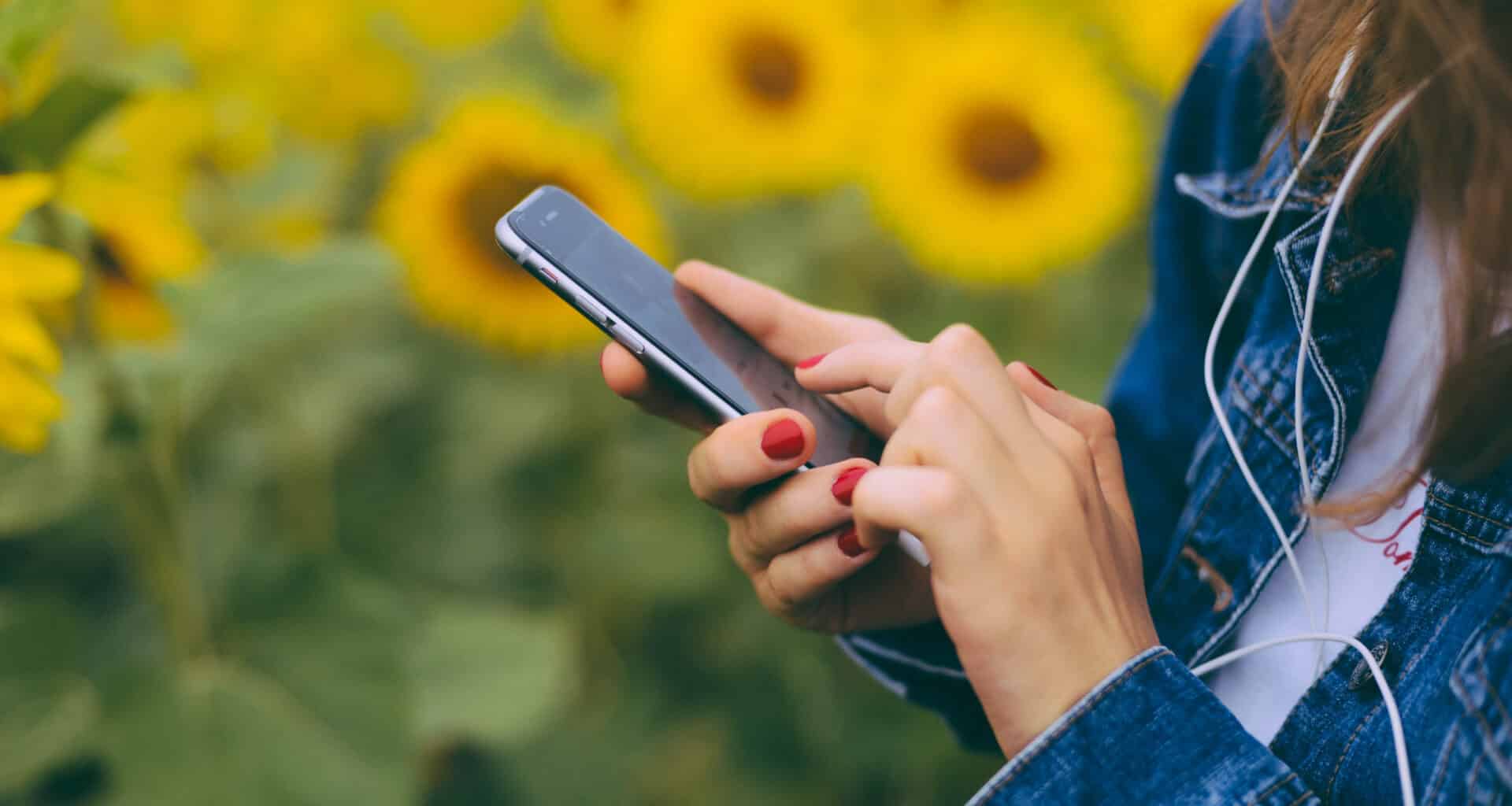 Mulher usando um iPhone com girassóis ao fundo