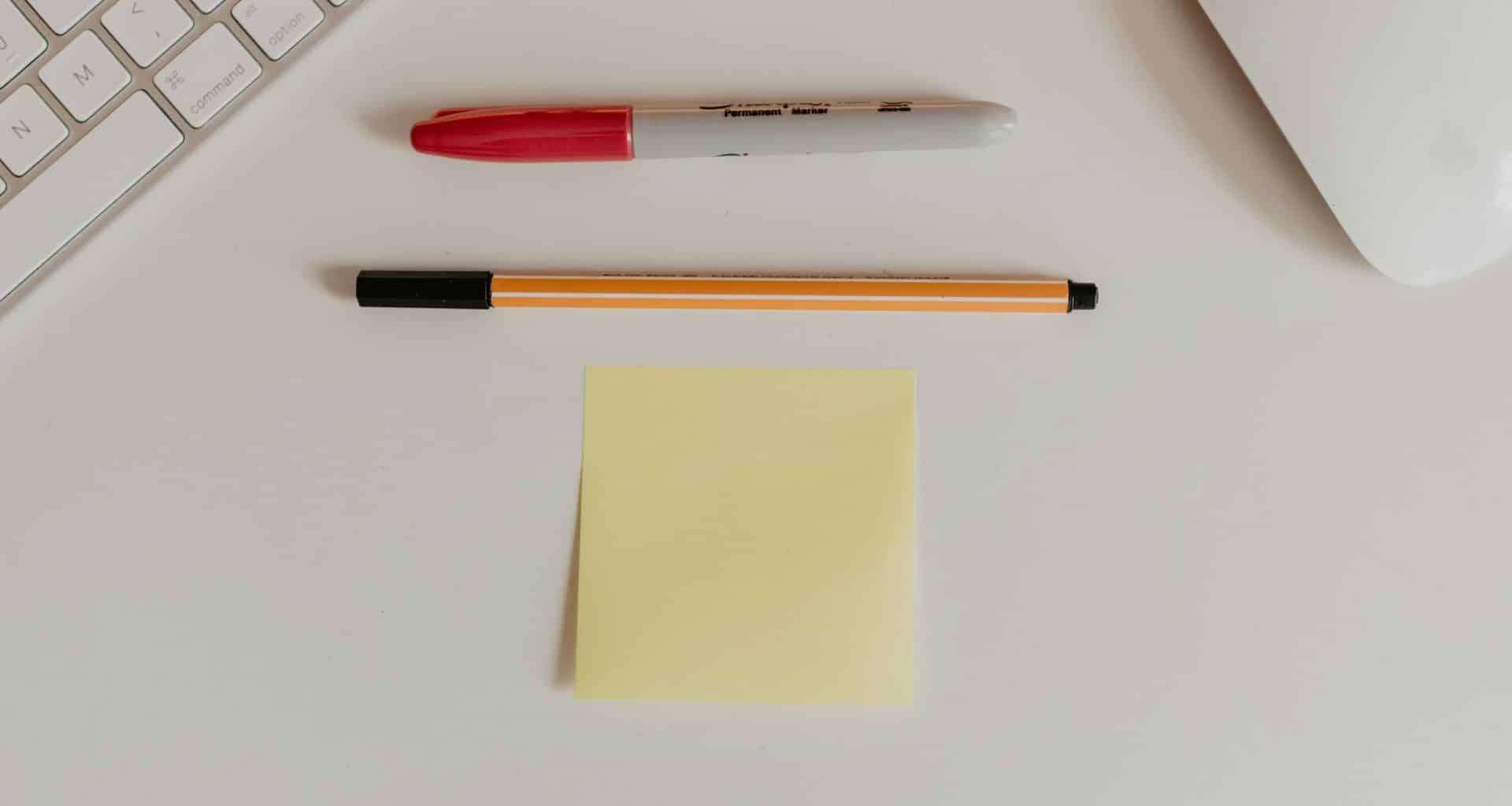 Post-it ao lado de canetas, teclado e mouse