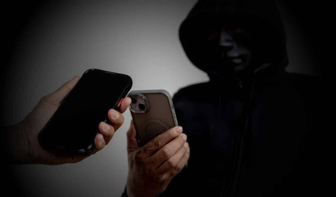Pessoa encapuzada segurando um iPhone próximo a outro (invasor, segurança, dados)