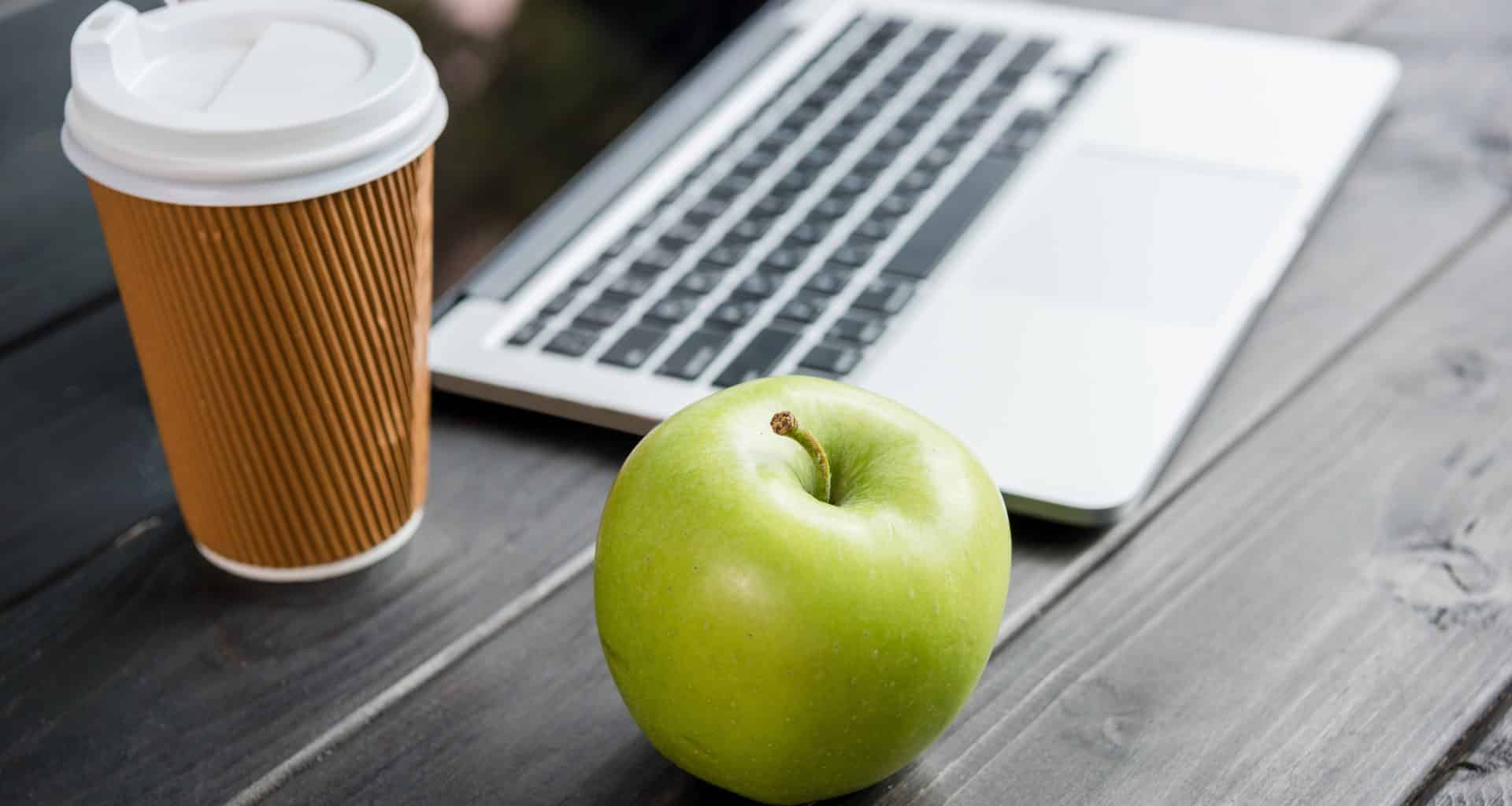 MacBook ao lado de copo com café e maçã verde