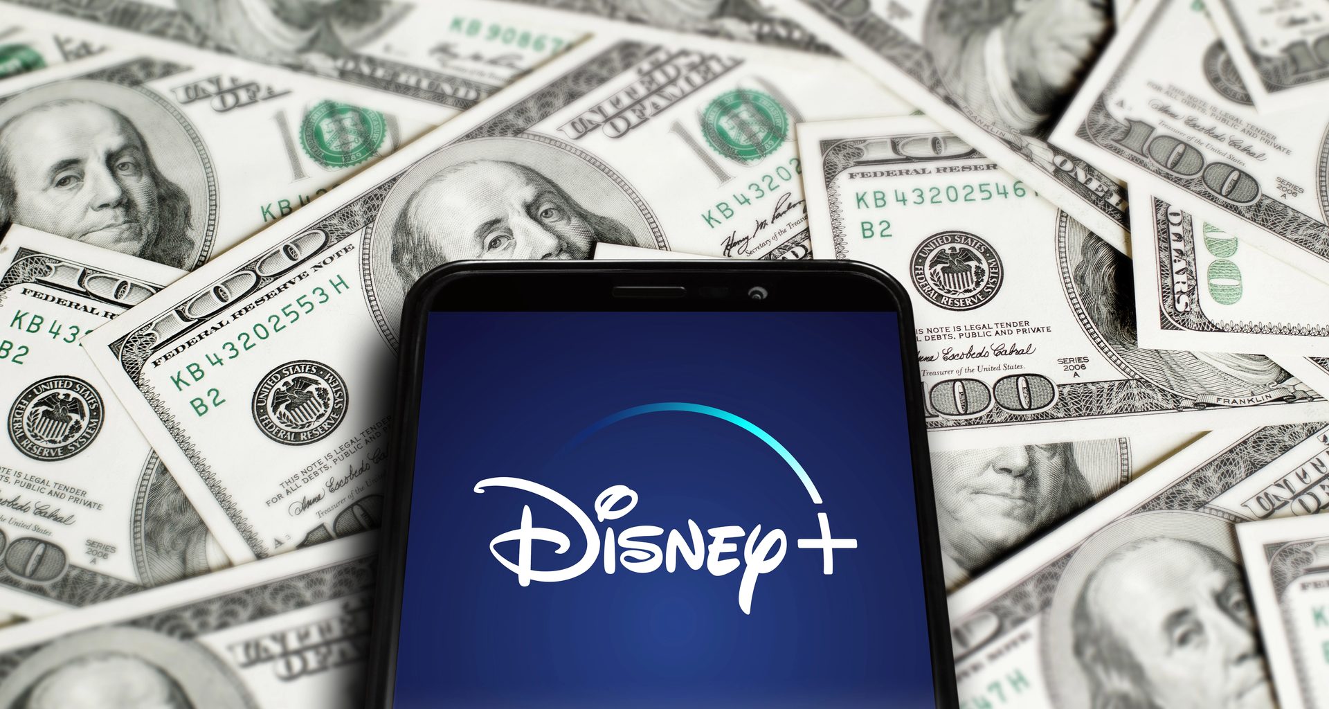 Logo do Disney+ em um telefone em cima de dinheiro (dólares)