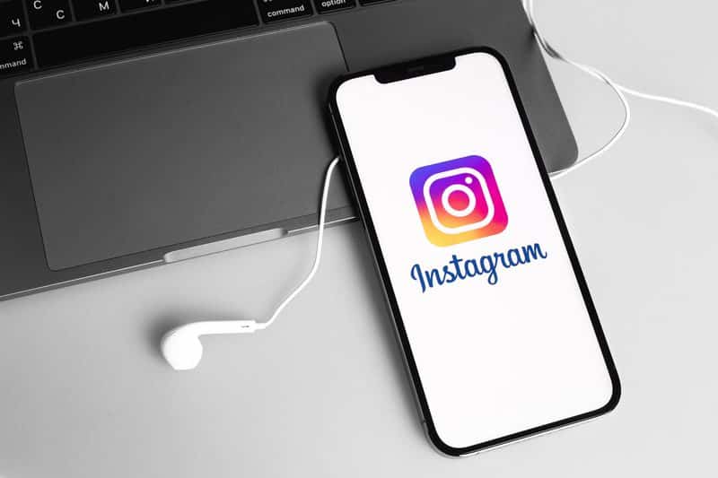 iPhone com o Instagram aberto, em cima de um Mac e com fios de fones ao lado