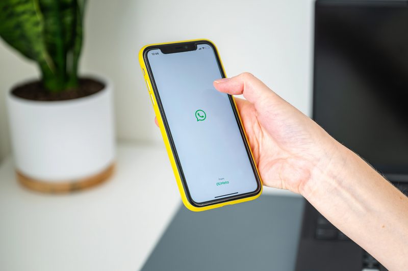 Mão de mulher segurando um iPhone com o logo do WhatsApp
