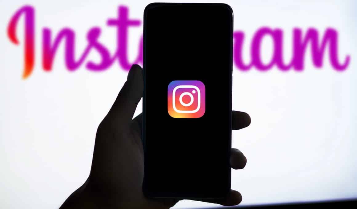 Mão segurando telefone com o ícone do Instagram e marca da rede social ao fundo