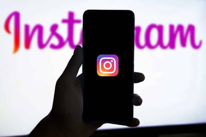 Mão segurando telefone com o ícone do Instagram e marca da rede social ao fundo