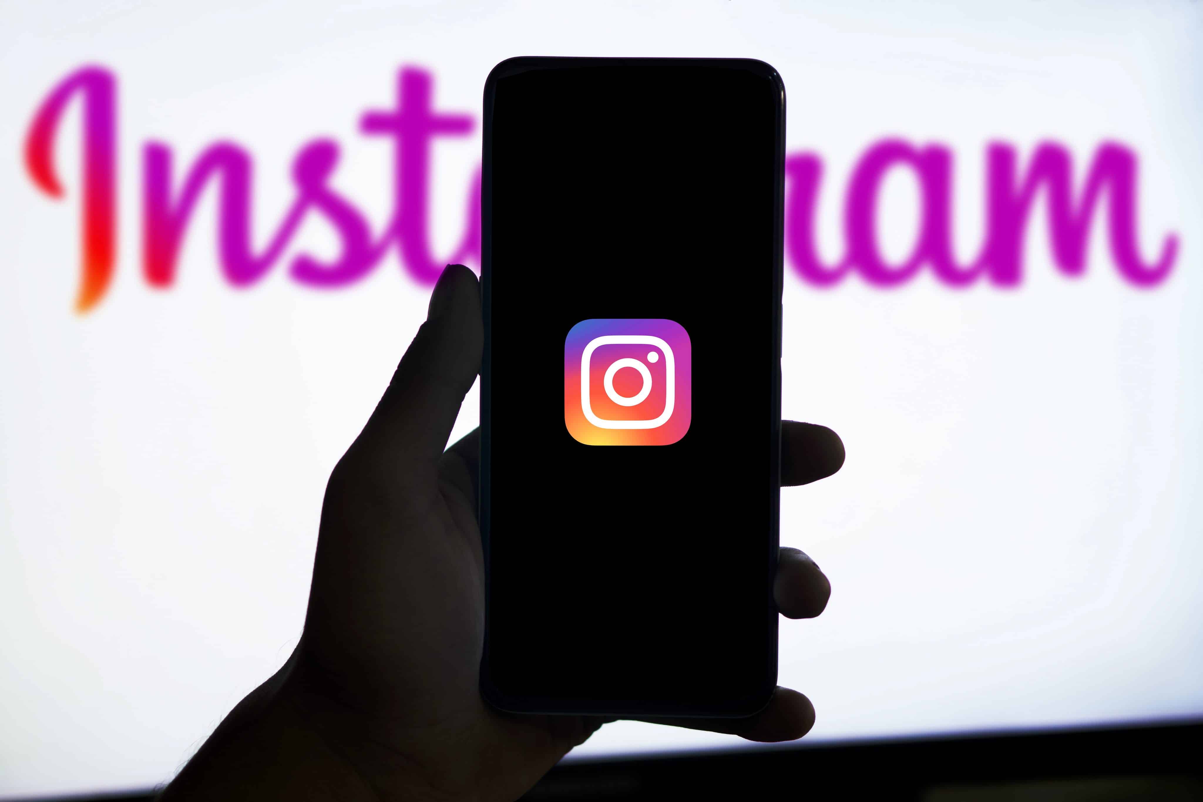 Mão segurando telefone com o ícone do Instagram e marca da rede social ao fundo