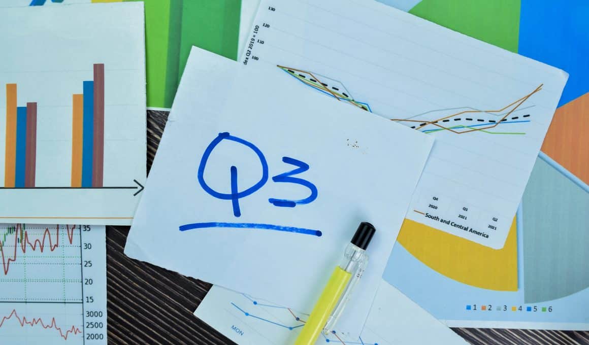 Anotação em um papel com Q3 (referência ao trimestre do ano) com diversos papéis com gráficos em cima de uma mesa