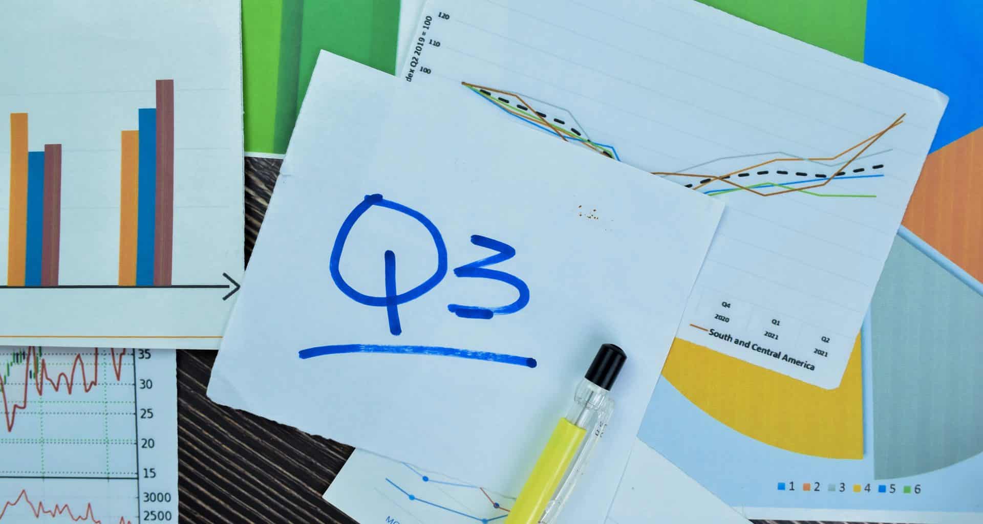 Anotação em um papel com Q3 (referência ao trimestre do ano) com diversos papéis com gráficos em cima de uma mesa