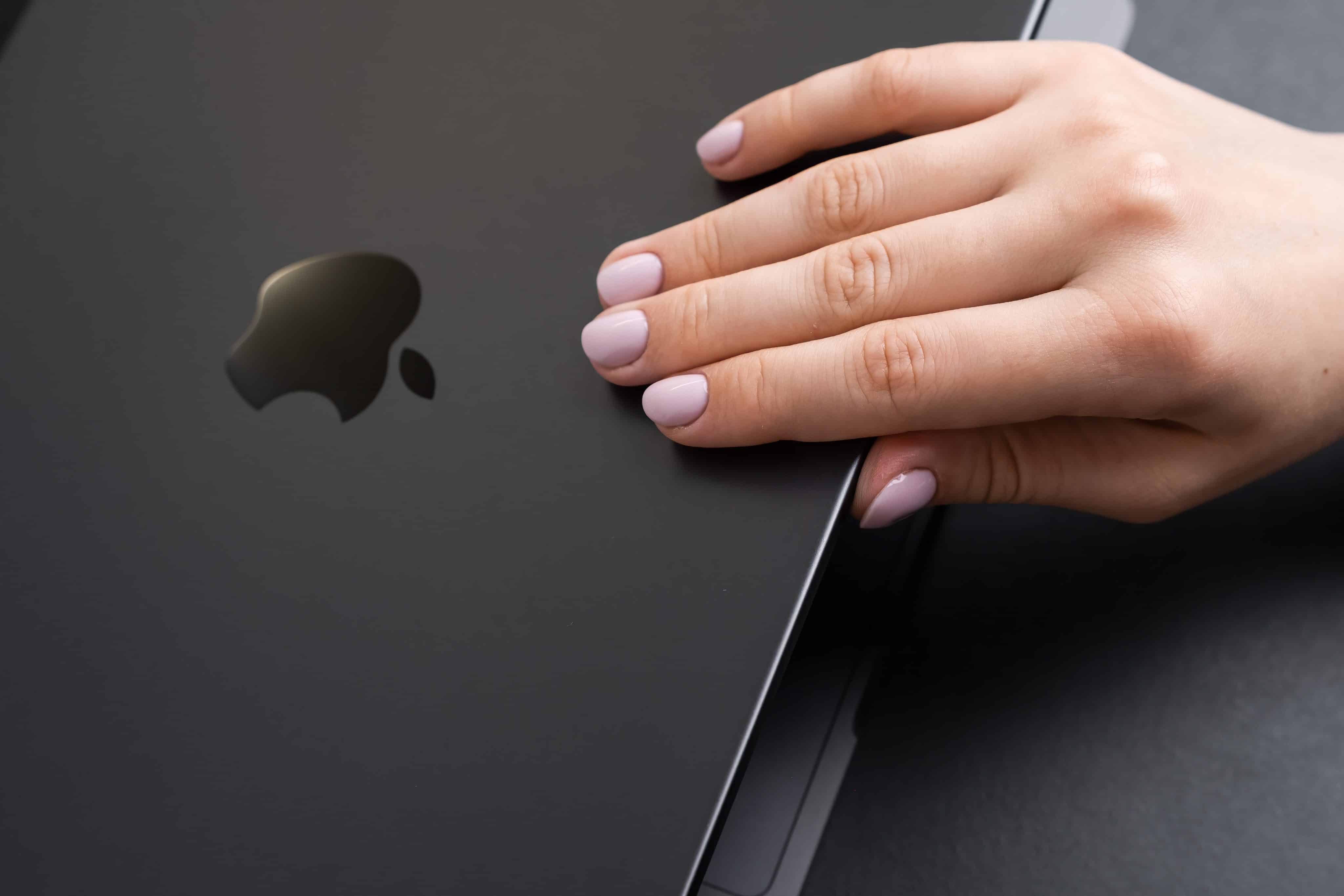 Close-up de uma mão de mulher abrindo a tampa de um MacBook Pro