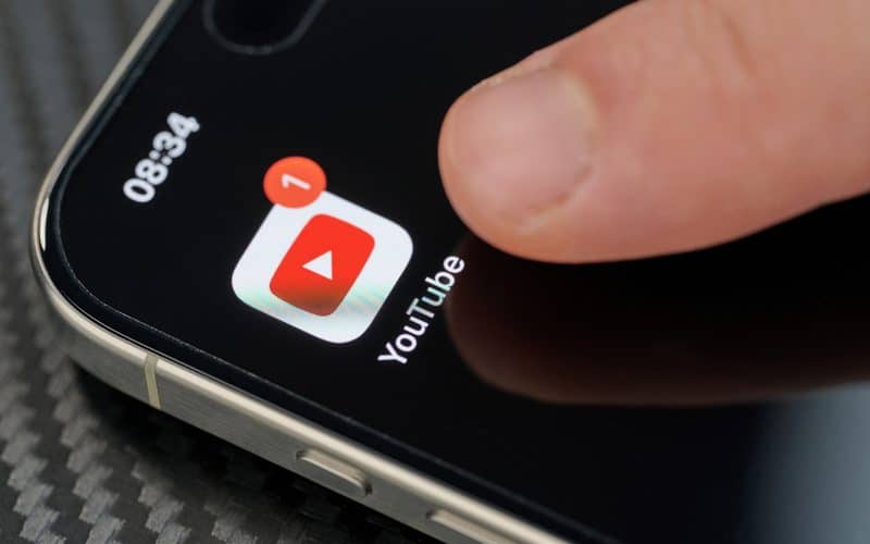 Dedo tocando no ícone do app do YouTube num iPhone