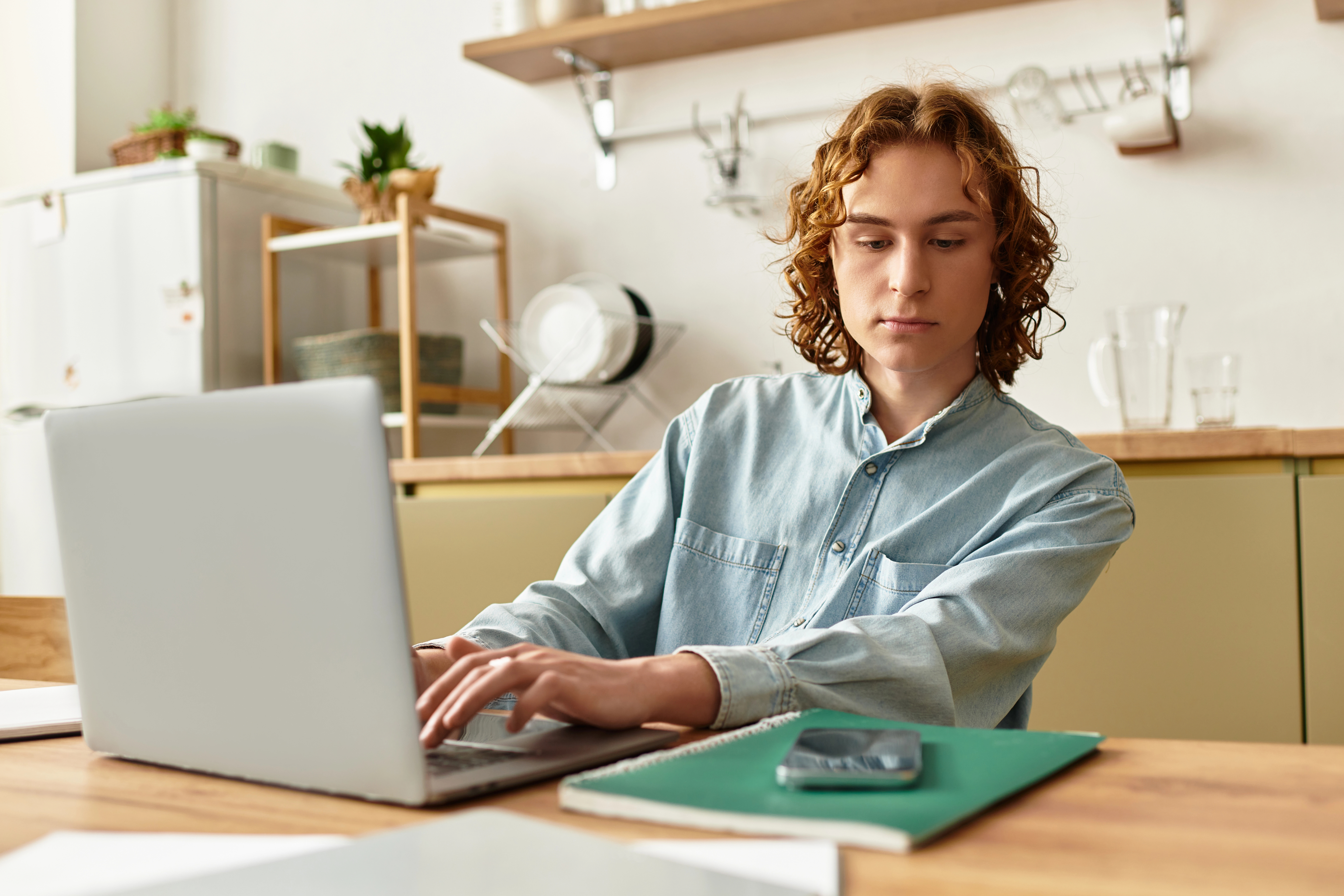Homem usando um computador e olhando para um telefone em cima da mesa